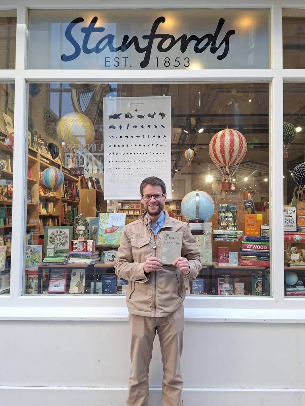 James Merriman holding a copy of 'The Kindness of Strangers' outside Stanfords in London